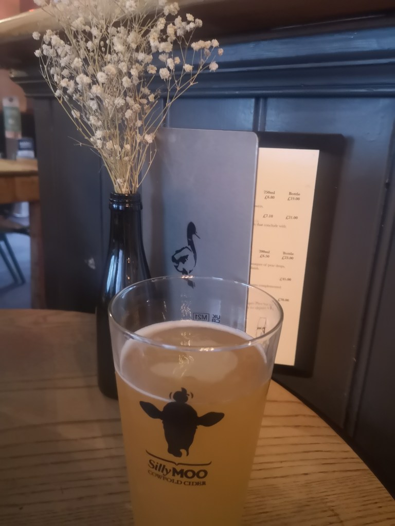 Partially drank pint of silly moo cider in front of the menu for The Mucky Duck